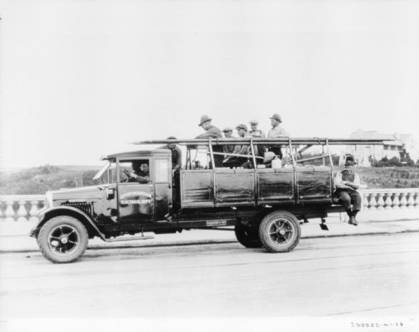 A group of men are in the back of a truck which is carrying equipment in Canada. Two men are sitting in the front seat, with one man driving the truck.