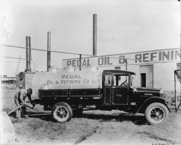 A man is standing at the back of a Regal Oil & Refining Co. Limited truck. In the background is a Regal Oil building.