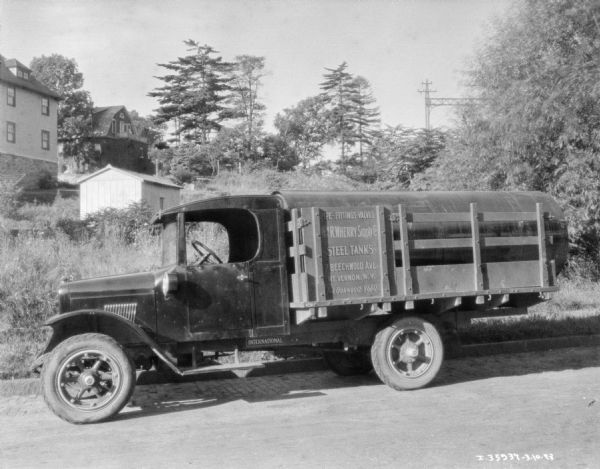 View across road towards a truck parked along the curb. The sign painted on the stack body on the side of the truck reads: "Pipe-Fittings-Valves, Wm. R. Wherry Supply Co., Steel Tanks." Buildings are on the hill in the background.