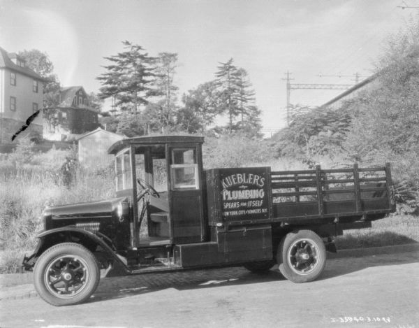 A Kuebler's Plumbing truck parked along the side of a road. The sign also reads: "Speaks for Itself, New York City, Yonkers, N.Y." Buildings are on the hill in the background.