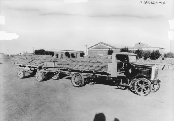 A grain delivery truck pulling a trailer. Sacks of grain are stacked on the open truck bed and the trailer.