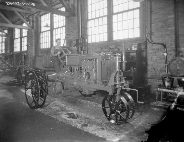 A man is sitting on a Farmall tractor in a factory.