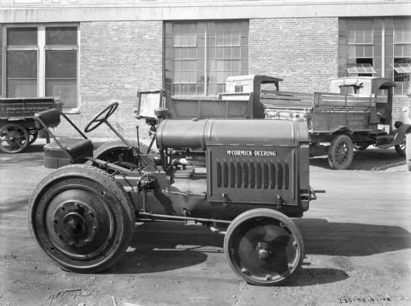 Right side view of an industrial tractor parked outdoors. There are trucks parked in the background near a brick building. The tires read: "Heavy Duty Goodyear Cushion."