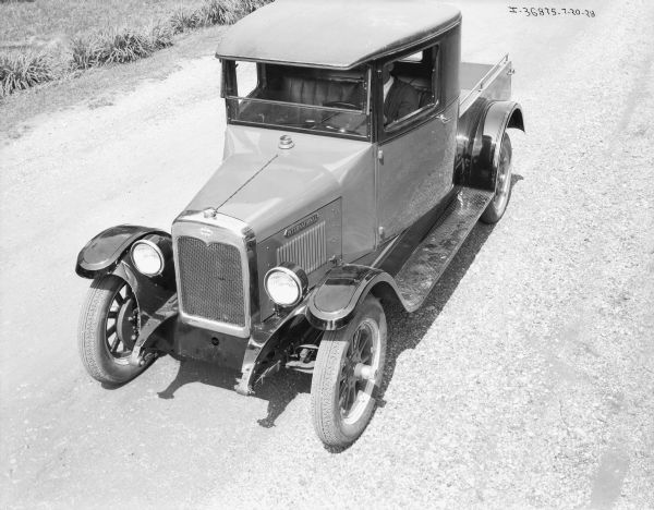 Slightly elevated view from front left of a truck parked on a gravel road. A man is sitting in the driver's seat, and the truck bed is open. On the front above the grill is the International triple diamond logo. The truck has Firestone tires.
