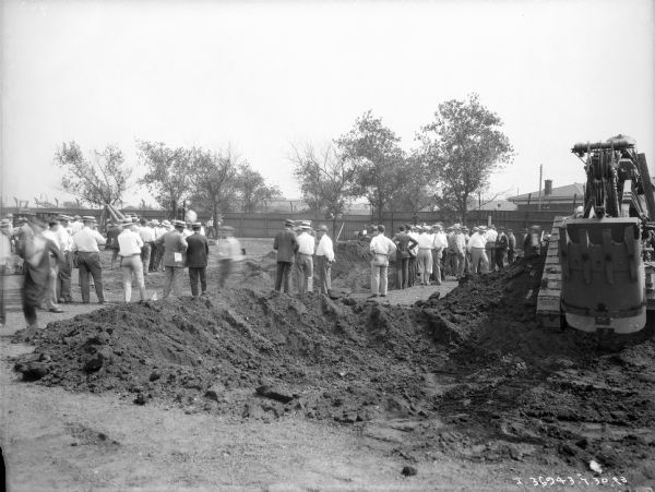 View towards groups of men gathered around machinery to watch demonstrations.