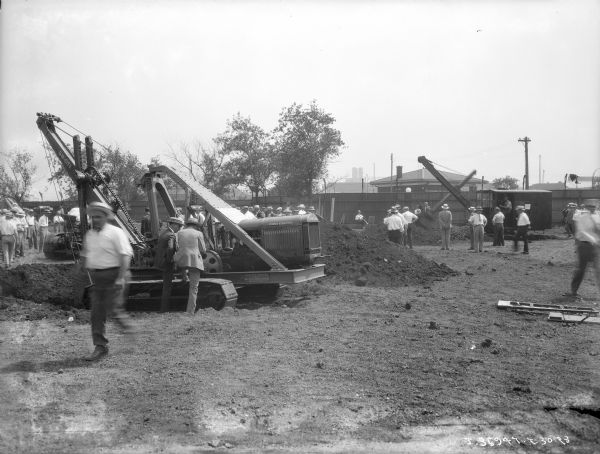 View towards groups of men gathered around machinery to watch demonstrations.
