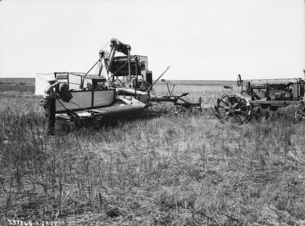 A man is holding a sack and standing next to a McCormick-Deering harvester-thresher in a field.