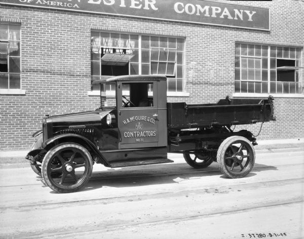 View across street towards a truck parked in font of a brick building. The sign painted on the driver's side door reads: "H.A. McGuire & Co. Contractors No. 31."