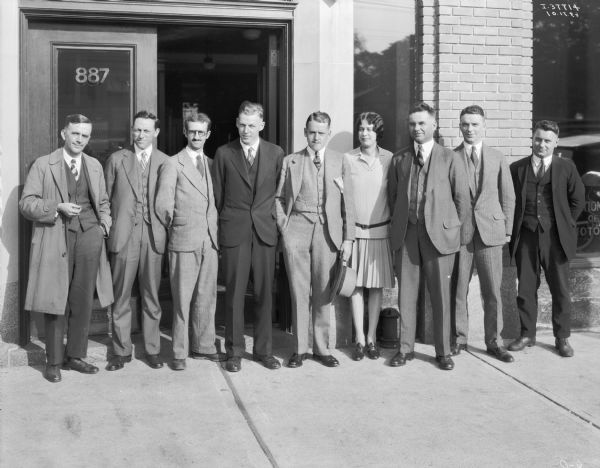 Group portrait of employees posing on the sidewalk in front of a dealership.