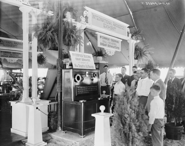 A group of men and boys are looking at an exhibit at a fair. A sign in the center reads: "This exhibit shows one of the many exciting factory tests of the steel balls used in New Departure Ball Bearings and proves the uniform high quality of the balls and bearings."