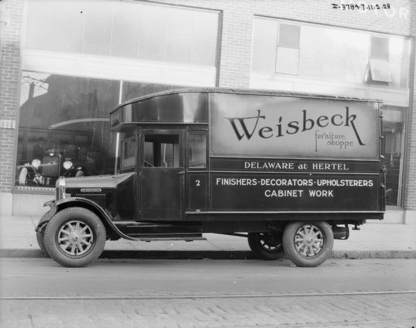 View across street towards a Weisbeck Furniture Shoppe truck parked along the curb in front of a building.