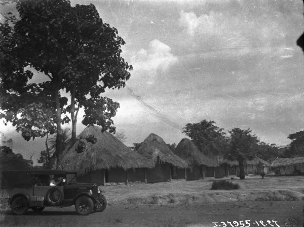 View towards a man sitting in an International truck. In the background are thatched roof buildings.