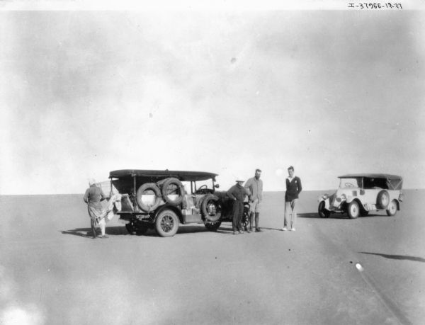 View across sand towards a group of men standing near two trucks in the Sahara Desert.