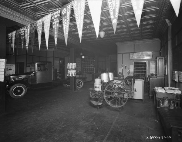 View of a display floor in a dealership, with banners hanging from the ceiling in the foreground. A truck is on the left, and machinery is in front of a counter in the center.