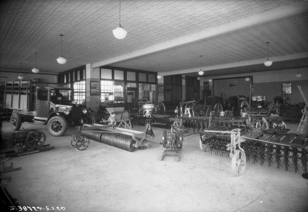 View of a truck, tractor, agricultural implements, cream separators and other items on display on the floor of a dealership.