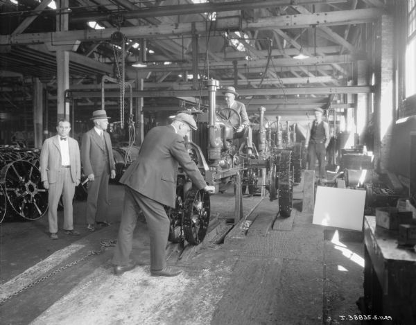 A group of men wearing suits are looking at a Farmall tractor on an assembly line.