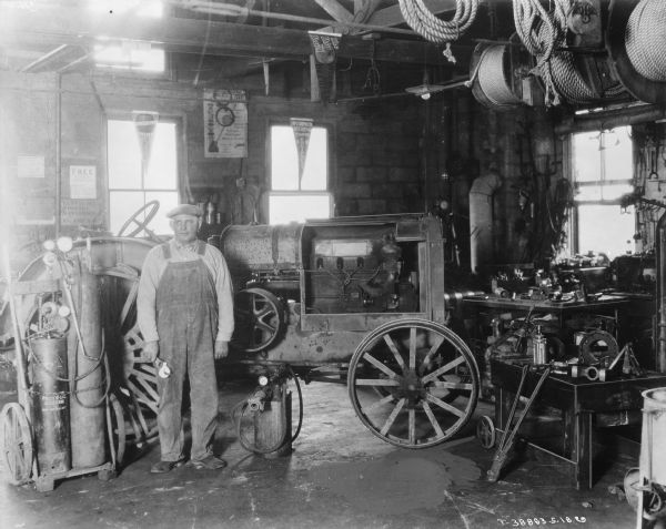 A man is standing in a repair shop at a dealership holding a wrench in one hand. Behind him is a Farmall tractor.
