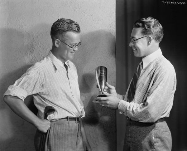 Two men are admiring a trophy from McCormick Club championship. The man on the left is holding a golf club, and the man on the right is holding the trophy.