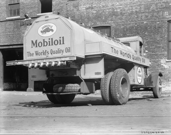 Three-quarter rear view of right side of a Gargoyle Mobiloil delivery truck parked in front of a brick building. The truck has an Illinois license plate.