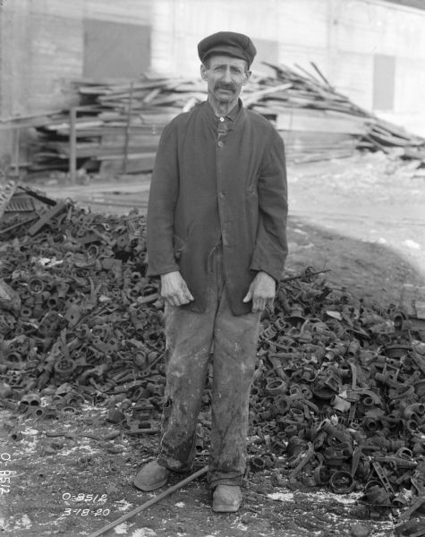A factory worker is standing in front of a pile of scrap parts in a factory yard — most likely at International Harvester's Osborne Works.