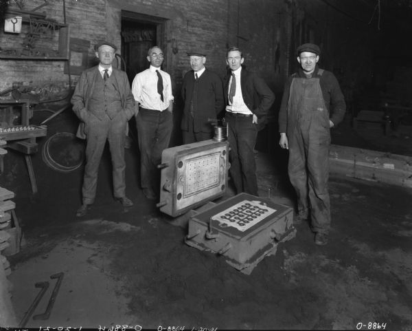Five men are standing in a finishing room. On the floor in front of them is a form for casting metal parts.