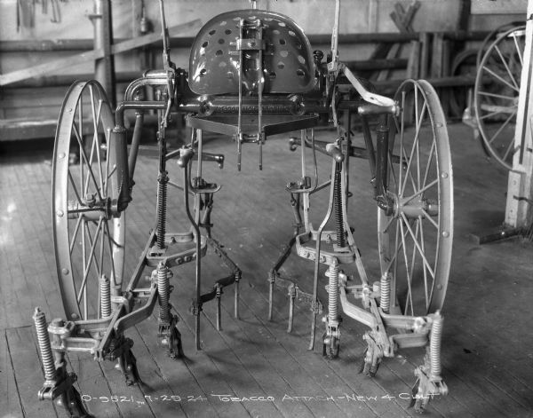 Rear view of a cultivator with a tobacco attachment on a factory floor. The seat is pushed up.