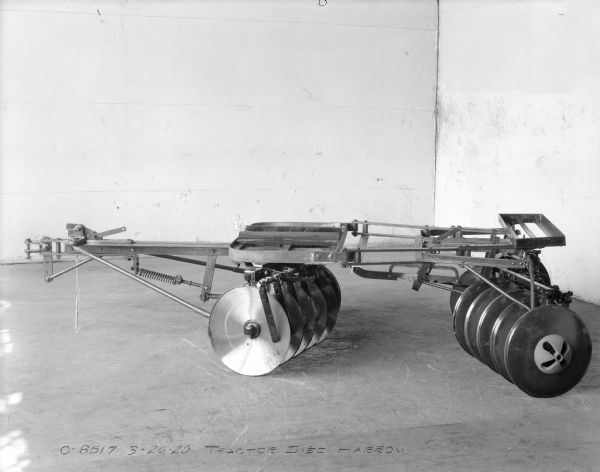 Side view of a tractor disc harrow set up on the floor in the corner of a room.
