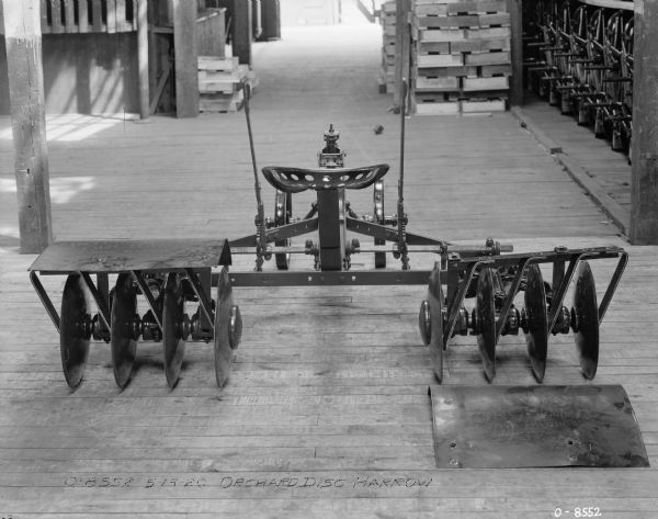Rear view of an orchard disc harrow set up on a wood floor in a large room.