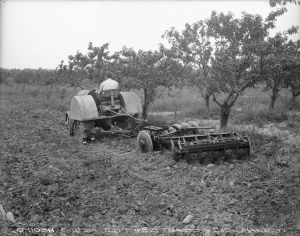 Rear view of a #8B, 5 1/4 ft. disk harrow being pulled by a man on a tractor.