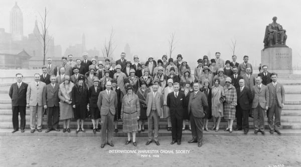 Outdoor group portrait of men and women in the McCormick Works' choral society. In the background on the right is a statue of Abraham Lincoln. In the background on the left are tall buildings in downtown Chicago.