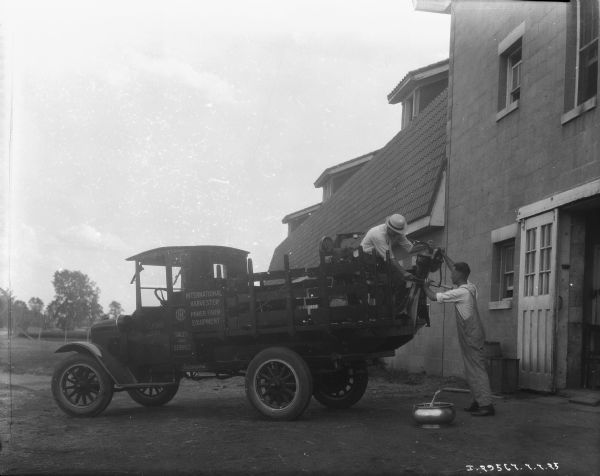 A salesman with a McCormick-Deering truck is showing a farmer a cream separator. The sign painted on the driver's side door reads: "Helm Bros. Elgin." There is a large barn behind the truck.