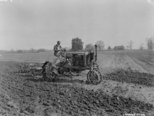 View towards a man using a Farmall tractor using a disk harrow for spring ground preparation.