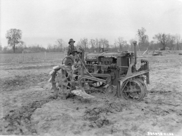 View across field towards a man using a Farmall tractor to pull a planter.