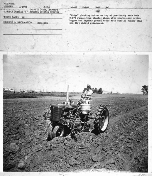 Three-quarter view from front left towards a man driving a Farmall C tractor in a field.
Subject: "Farmall C - C-277 & C-278 (Forward Mounted) Cotton Tractor." Where Taken: "SE." Information with photograph reads: "'Ridge' planting cotton on top of previously made beds. C-278 runner-type planter shown with single-seed cotton hopper and regular ground tools with special runner wing and dirt shield attachment."