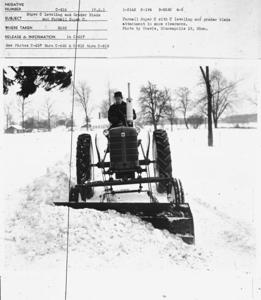 Front view of man driving tractor in snow.
Subject: "Super C Leveling and Grader Blade and Farmall Super C." Where Taken: "MidW." Information with photograph reads: "Farmall Super C with C leveling and grader blade attachment in snow clearance. Photo by Travis, Minneapolis 19, Minn."