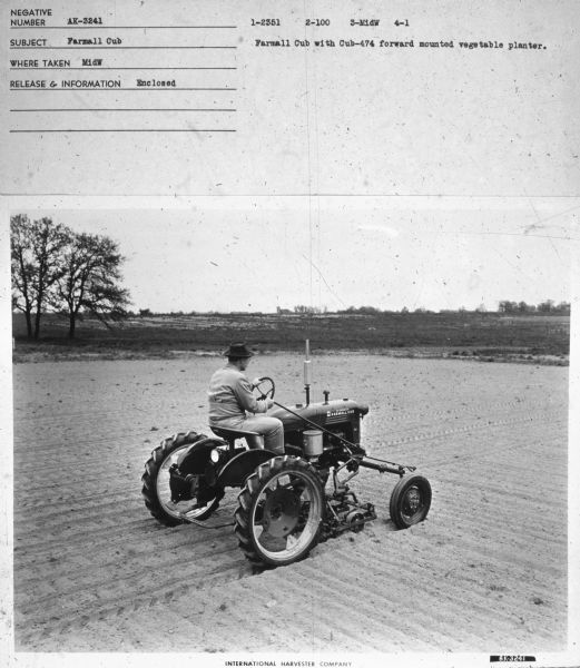 Three-quarter view from right rear of a man driving a Farmall Cub.
Subject: "Farmall Cub." Where Taken: "MidW." Information with photograph reads: "Farmall Cub with Cub-474 forward mounted vegetable planter." 