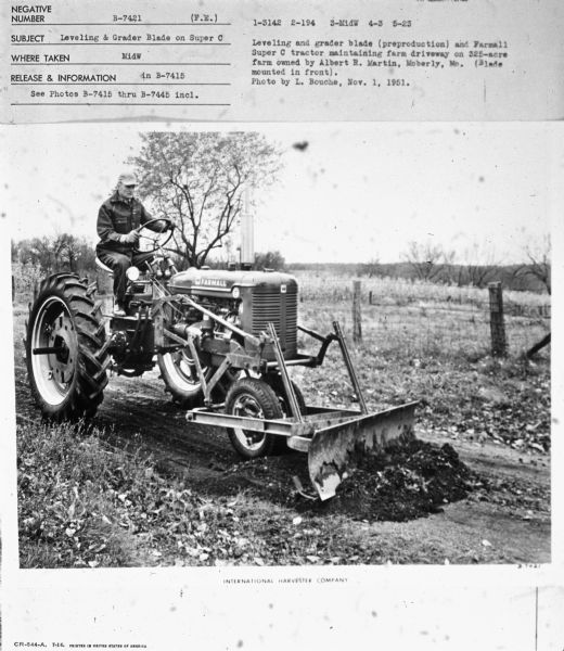 Three-quarter view from front right of a man driving a Farmall Super C tractor in a field.
Subject: "Leveling & Grader Blade on Super C." Where Taken: "MidW." Information with photograph reads: "Leveling and grader blade (preproduction) and Farmall Super C tractor maintaining farm driveway on 325-acre farm owned by Albert R. Martin, Moberly, Mo. (Blade mounted on front). Photo by L. Bouche, Nov. 1, 1951."