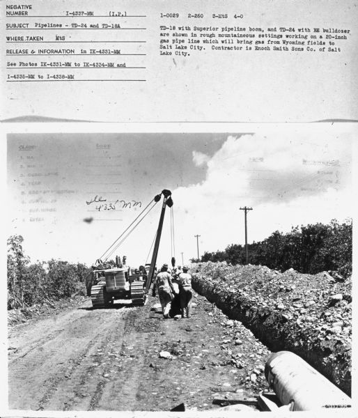 Rear view of men working to install gas pipelines. 
Subject: "Pipelines — TD-24 and TD-18A." Where Taken: "MtS." Information with photograph reads: "TD-18 with Superior pipeline boom, and TD-24 with BE bulldozer are shown in rough mountaineous settings working on a 20-inch gas pipe line which will bring gas from Wyoming fields to Salt Lake City. Contractor is Enoch Smith Sons Co. of Salt Lake City."