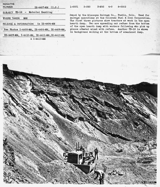 View looking down at men working on and around a TD-18A crawler tractor.
Subject: "TD-18 — Material Handling." Where Taken: "MtS." Information with photograph reads: "Owned by the Minnequa Salvage Co., Pueblo, Colo. Used for salvage operations at the Colorado Fuel & Iron Corporation. The first three pictures show tractors at work in the open hearth dump. Two are spreading out refuse from the bottom of the open hearth dump with workers following who pick up pieces of metal mixed with refuse. Another TD-18 is shown in background working at the bottom of abandoned dump."
