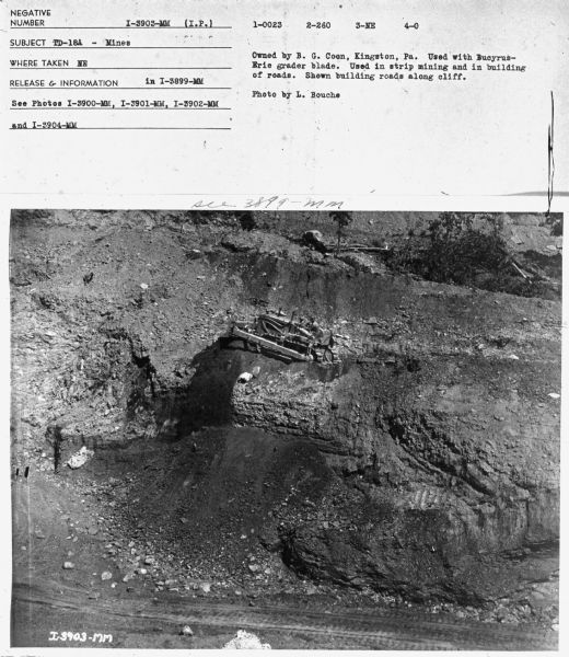 View looking down at a man using a TD-18 to build roads along a cliff.
Subject: "TD-18A — Mines." Where Taken: "NE." Information with photograph reads: "Owned by B.G. Coon, Kingston, Pa. Used with Bucyrus-Erie grader blade. Used in strip mining and in building of roads. Shown building roads along cliff. Photo by L. Bouche."