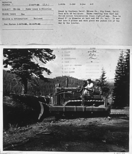 Right side view of a man driving a TD-14A crawler tractor.
Subject: "TD-14A — Power Lines & Utilities." Where Taken: "Pac." Information with photograph reads: "Owned by Southern Calif. Edison Co. Big Creek, Calif. Used with BE bulldozer. Shown removing tree that had fallen across transmission lines right-of-way. Tree is about 6' in diameter at butt and 250 ft. tall. It was cut into 3 pieces and each piece was pushed out of the way by the tractor."