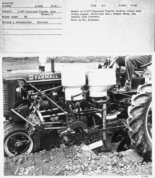 Side view of left side of a Farmall C tractor. A man (partially out of frame) is sitting on the tractor seat.
Subject: "C-277 Blackland Planter with Farmall C." Where Taken: "SE." Information with photograph reads: "Detail of C-277 Blackland Planter showing single seed cotton hopper, fertilizer unit, winged sweep, and special disk coverers. Photo by Wm. Eichmann."