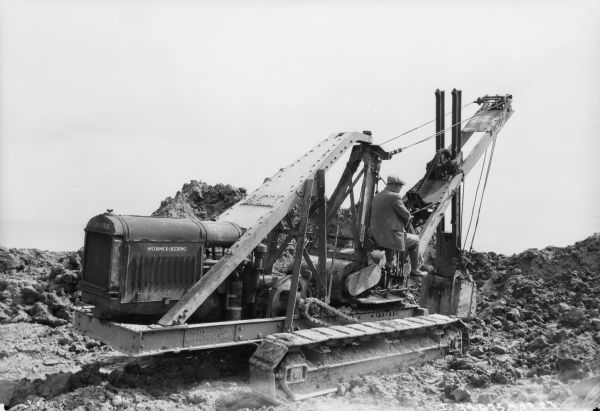 Right side view of a man operating a McCormick-Deering earthmover. The sign at the base reads: "Tractor Shovel, No. 713, Bay City Dredge Works, Bay City, Mich."