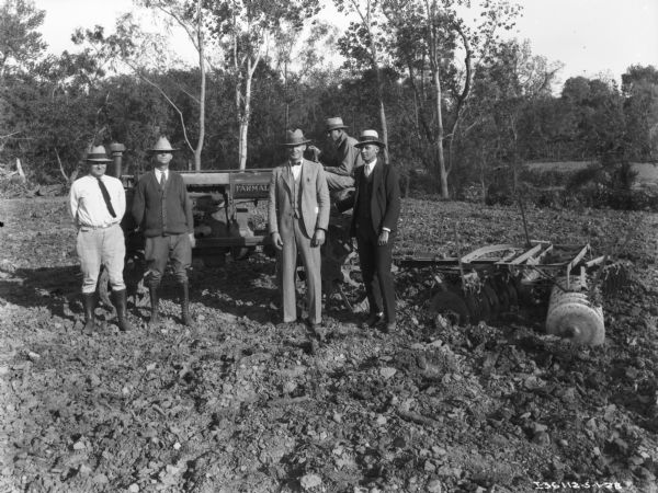 A group of men are posing in front of a man sitting on a Farmall tractor.
