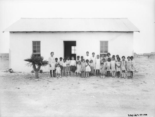 Group portrait of school children and teacher standing and posing in front of a school house in Mexico.
