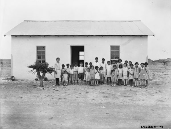 Group portrait of school children and teacher standing and posing in front of a school house in Mexico.