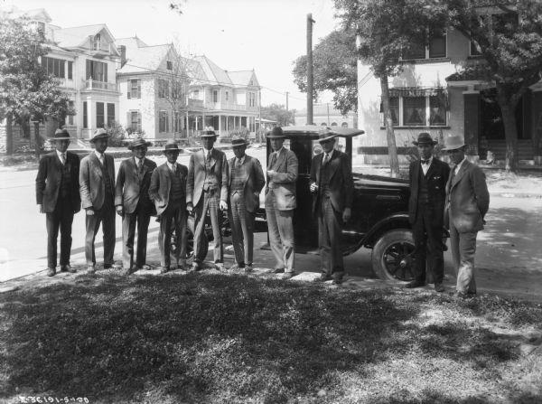 Outdoor group portrait of businessmen posing on the sidewalk in front of a truck parked along the curb.