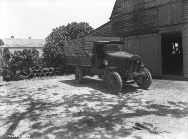 A man is sitting in the drivr's seat of a farm truck parked near a barn. The sign painted on the side of the truck bed reads: "R.&G. Riess, St. Bernard Parish."