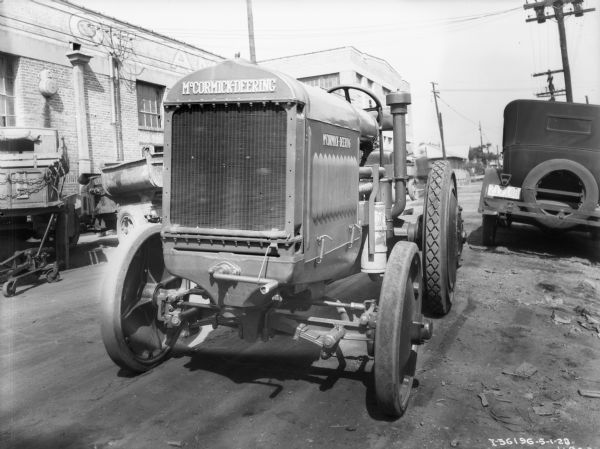 View of the front of a McCormick-Deering industrial tractor. An industrial building is in the background.