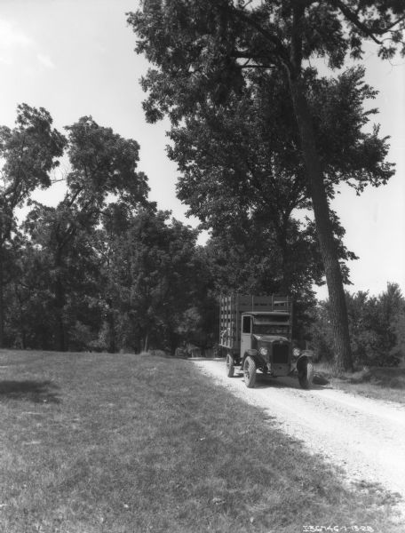 A man is driving a livestock truck down a country road. The truck has a stake body.